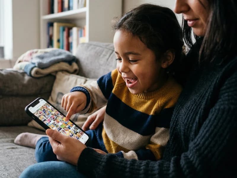 A child and parent looking at a phone together, the child pointing at a photo with delight